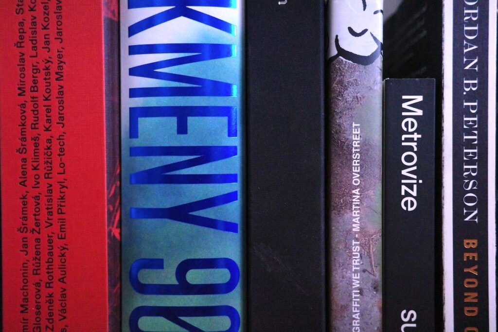 Na obrázku jsou knihy v knihovně. Kmeny 90, Architektura 58-89, Nádech nebo Metrovize od nakladatelství Big Boss.